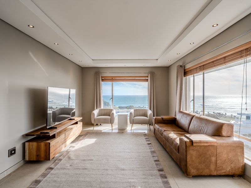 Bright and modern living room featuring large windows with expansive ocean views, recessed ceiling lighting, and neutral tiled flooring.