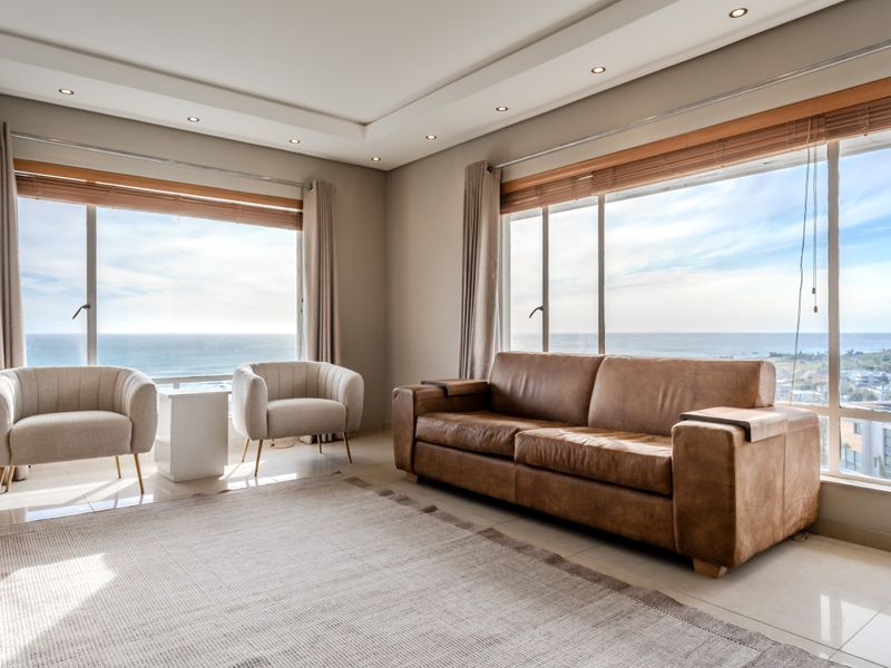 Bright and spacious living room featuring large windows with expansive ocean views, recessed ceiling lighting, and neutral tiled flooring.
