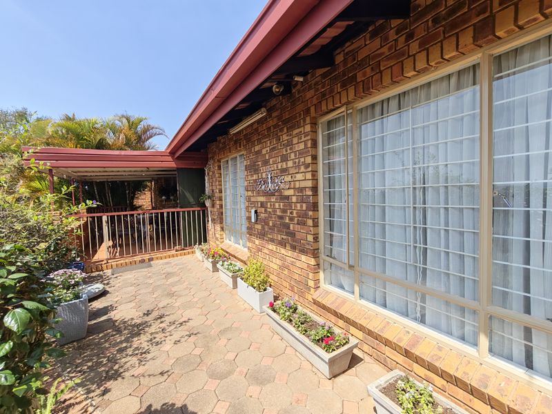 A well-maintained paved patio area featuring face brick exterior walls, metal security bars on windows, and a covered veranda section.