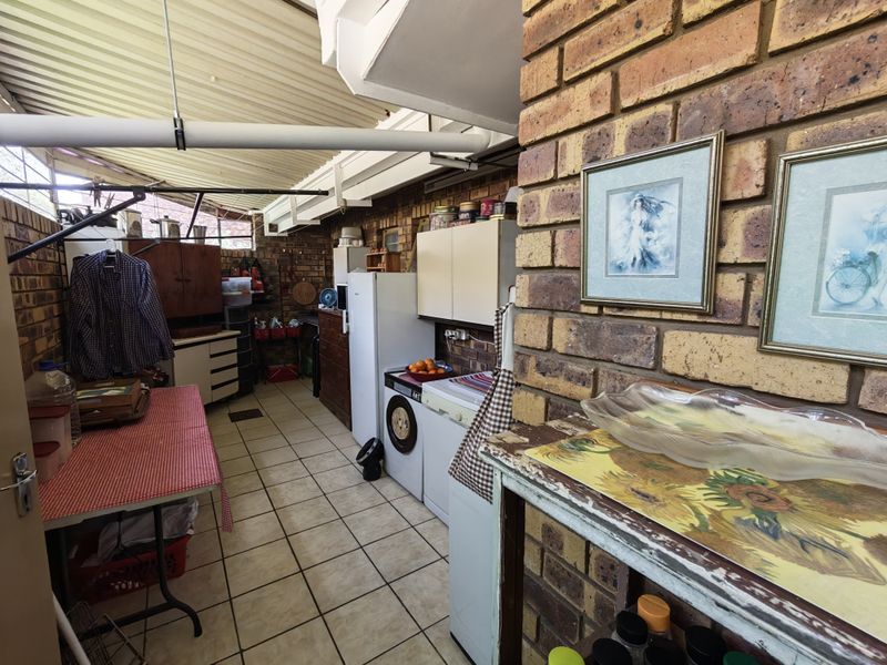 A functional laundry area featuring exposed brick walls, tiled flooring, and built-in cabinetry under a corrugated roof structure.