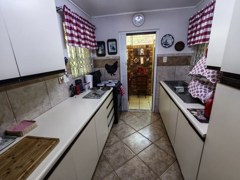 A functional galley-style kitchen featuring laminate countertops, tiled backsplash, and ceramic flooring, with direct access to an adjacent utility area.