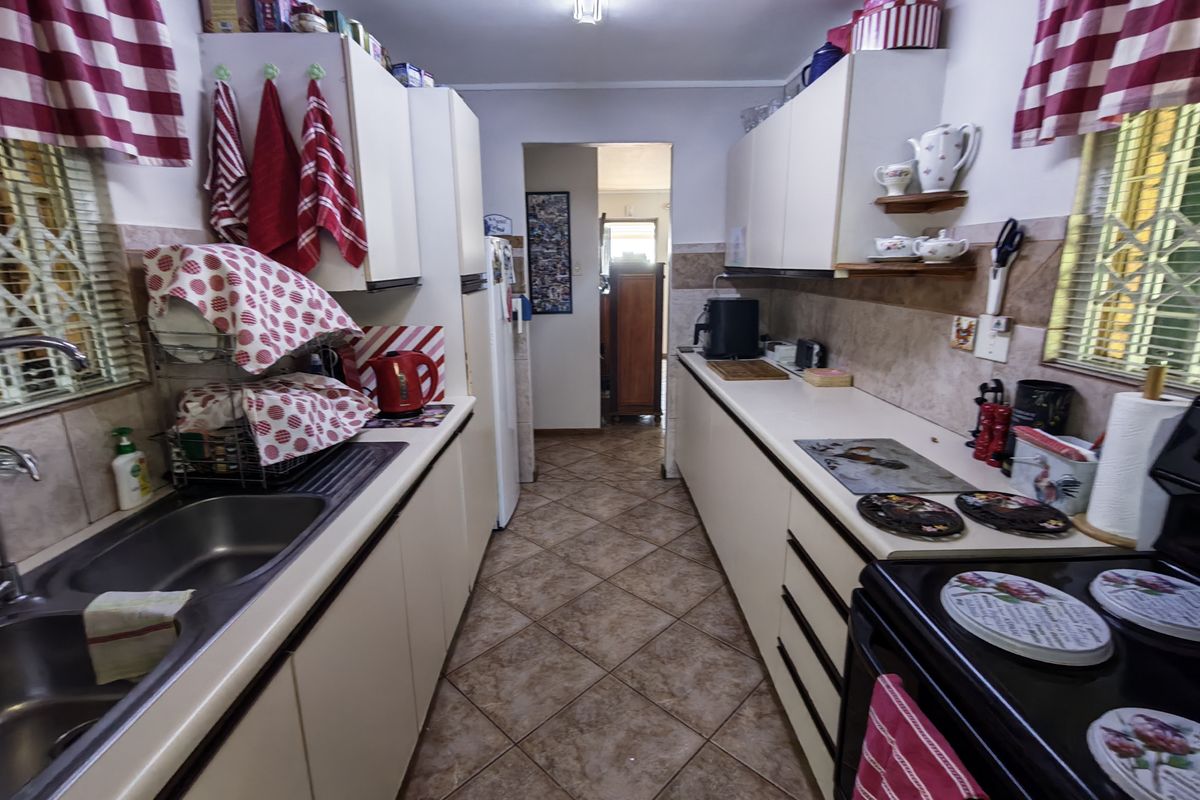A functional galley-style kitchen featuring tiled flooring, laminate countertops, a double bowl sink, and built-in cabinetry with a tiled backsplash.