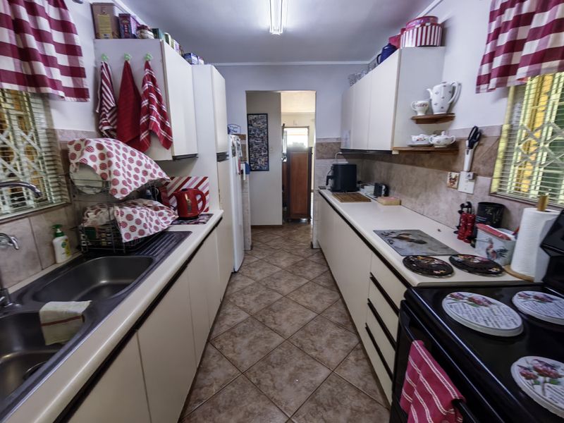 A functional galley-style kitchen featuring tiled flooring, laminate countertops, a double bowl sink, and built-in cabinetry with a tiled backsplash.