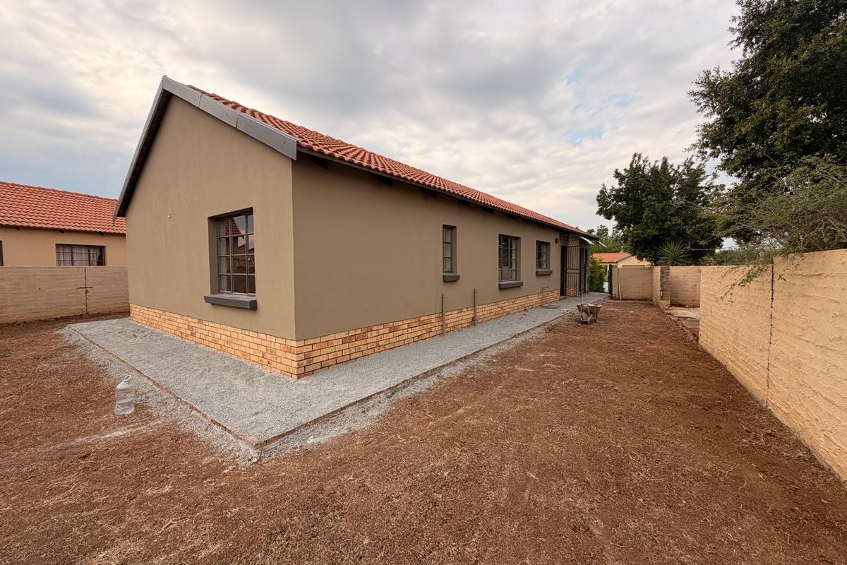 Rear view of a residential house featuring a terracotta tiled roof, plastered exterior walls with a brick plinth, and an unfinished garden area.