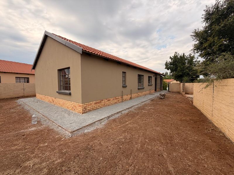Rear view of a residential house featuring a terracotta tiled roof, plastered exterior walls with a brick plinth, and an unfinished garden area.