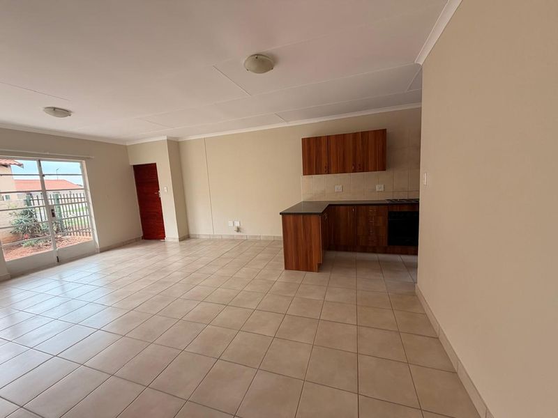 An open-plan living and kitchen area featuring tiled flooring, wood-finish cabinetry, built-in cooking appliances, and a sliding door leading to the exterior.