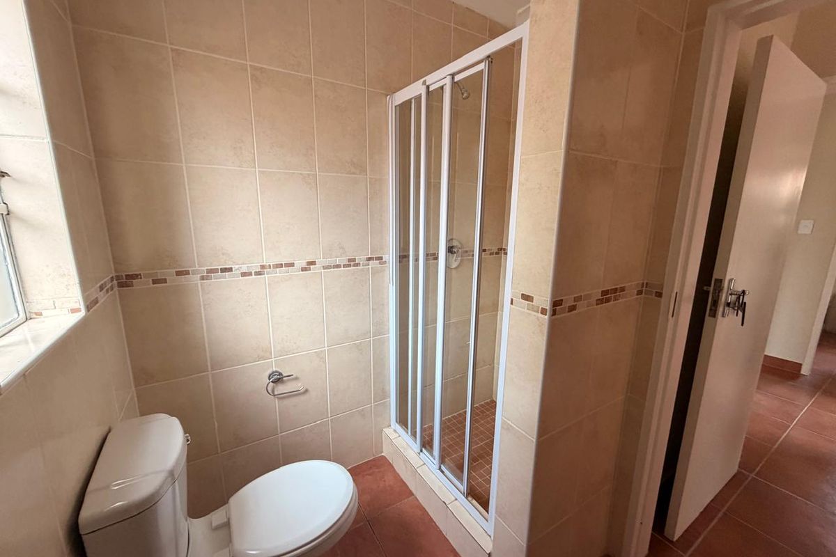 A functional bathroom featuring a tiled shower enclosure, toilet, and neutral wall tiling, offering a clean and practical space.