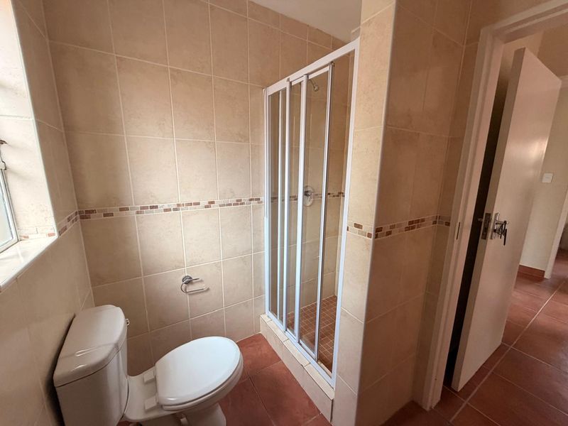 A functional bathroom featuring a tiled shower enclosure, toilet, and neutral wall tiling, offering a clean and practical space.