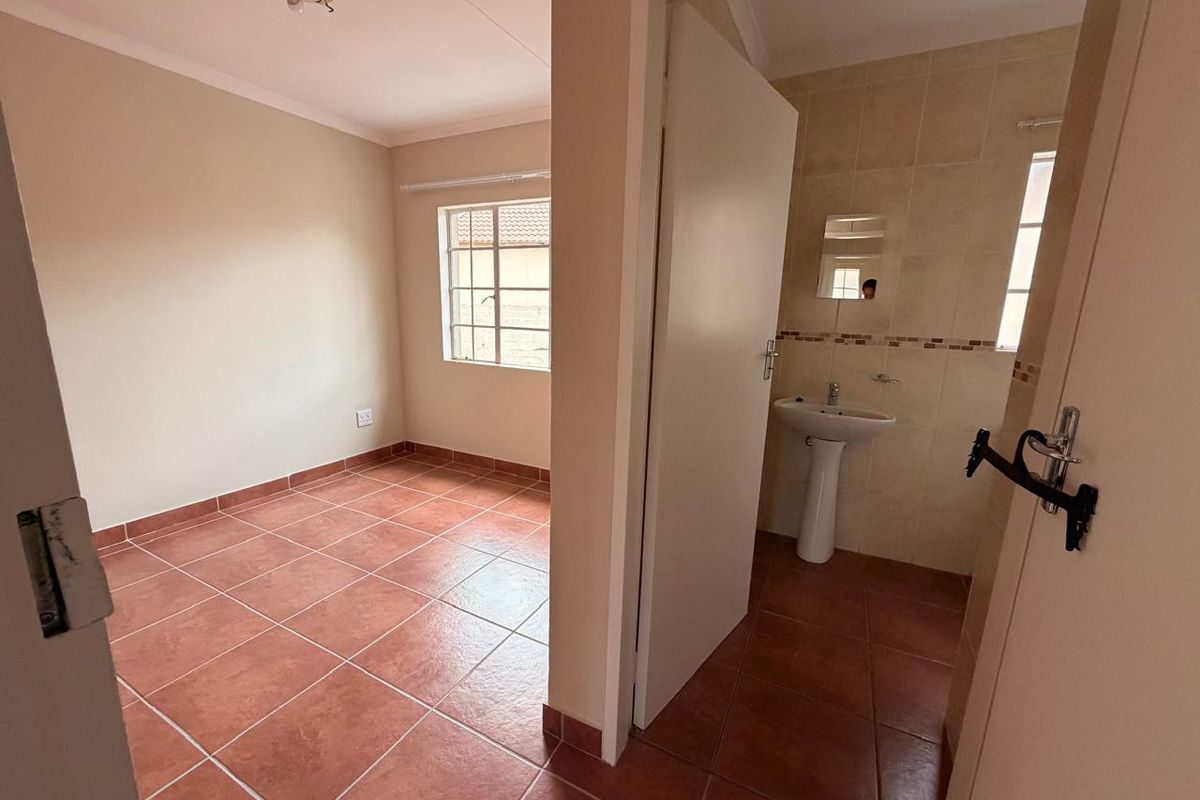 An empty bedroom featuring tiled flooring and an en-suite bathroom area with a pedestal basin and wall-mounted mirror.