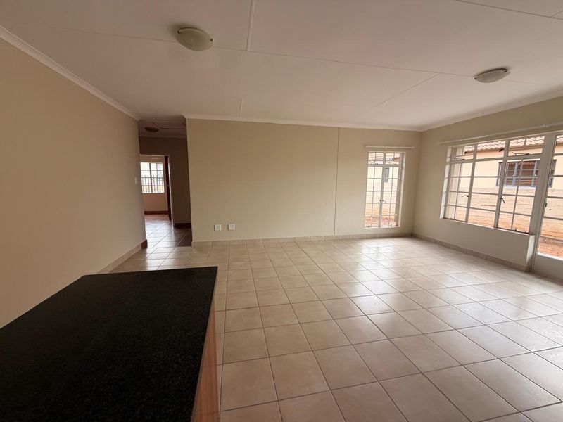 Spacious open-plan living area featuring neutral tiled flooring, large windows with security bars, and a granite-topped breakfast counter.