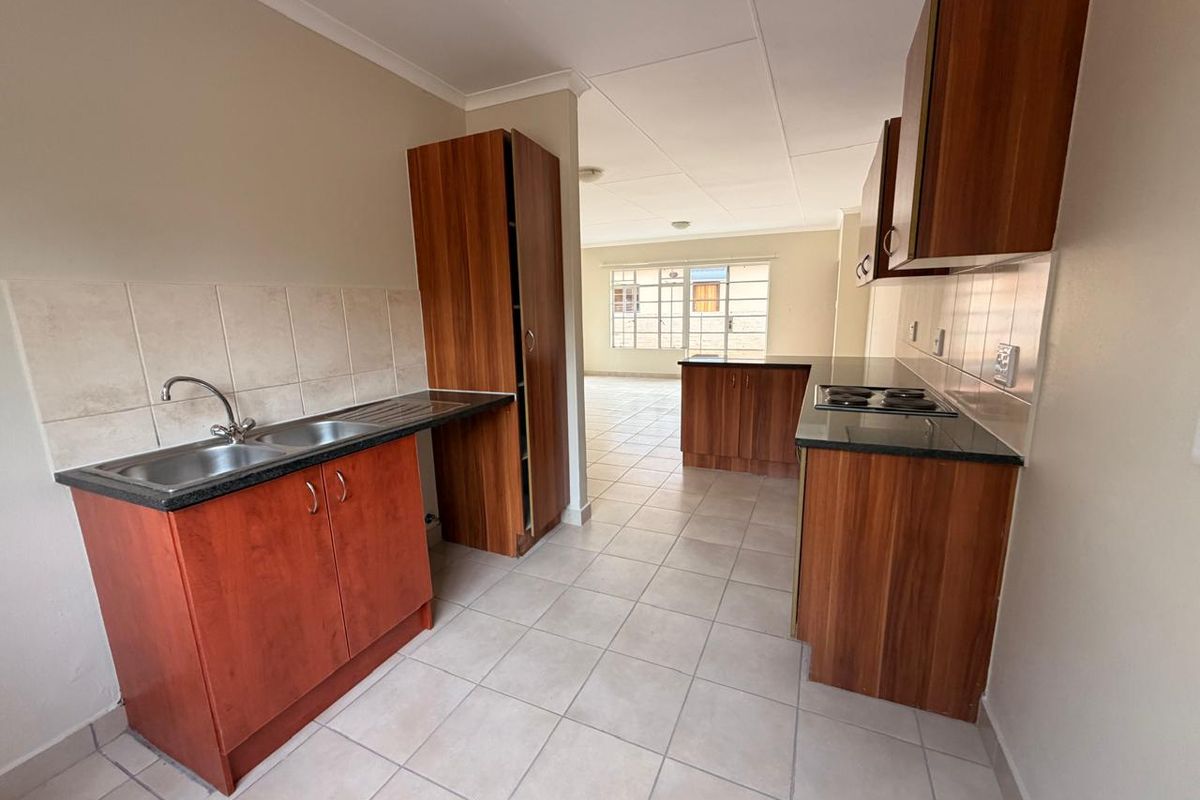 A functional kitchen featuring wood-finish cabinetry, granite countertops, a double sink, and an integrated electric hob, leading into an open-plan living area.