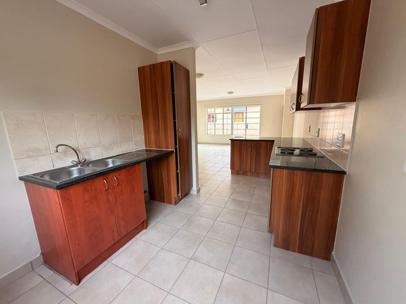 A functional kitchen featuring wood-finish cabinetry, granite countertops, a double sink, and an integrated electric hob, leading into an open-plan living area.