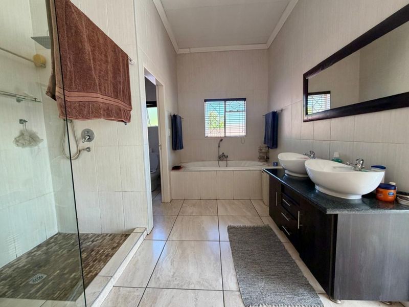 Spacious bathroom featuring a double vanity, built-in bathtub, and a separate glass-enclosed shower with neutral wall and floor tiling.
