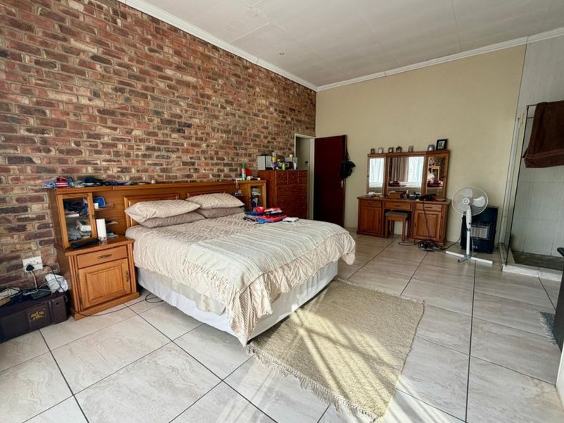 Spacious bedroom featuring an exposed brick feature wall, neutral tiled flooring, and coved ceiling details.