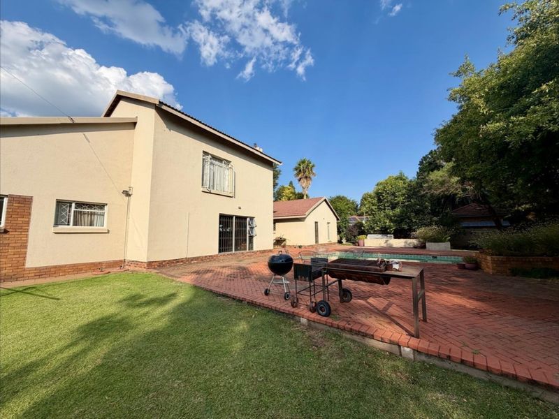 Rear exterior view featuring a brick paved patio, swimming pool, and well-maintained lawn area adjacent to the main house structure.
