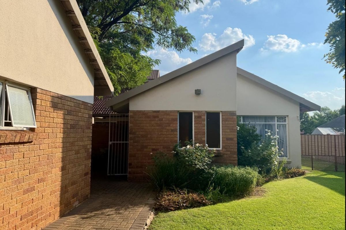 Rear view of the property featuring a brick facade, paved walkway, and well-maintained garden area with established landscaping.
