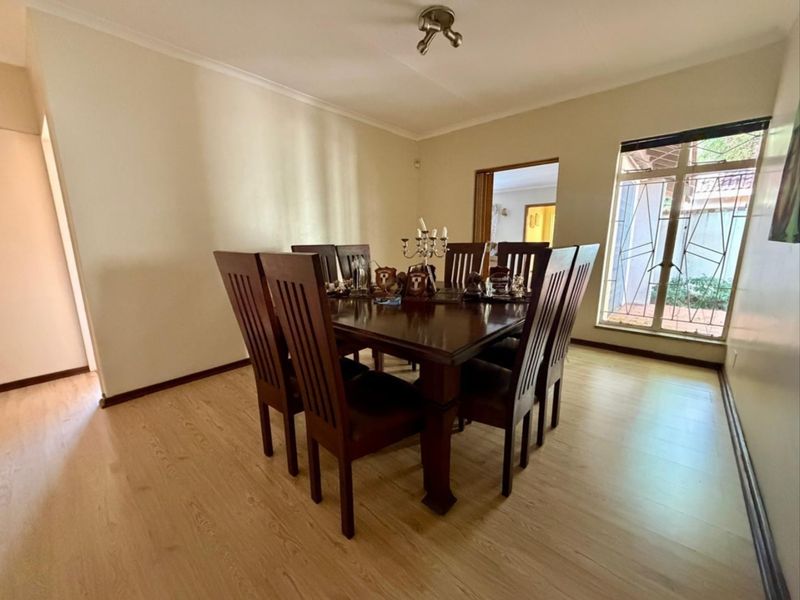 A dining room featuring light-toned laminate flooring, neutral walls, and a large window with a security gate, providing a functional space for meals.