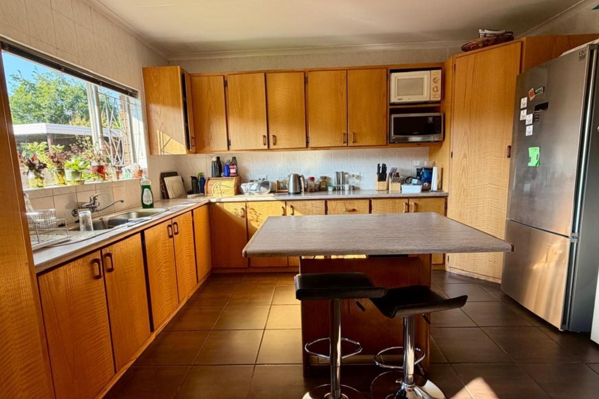 A functional kitchen featuring wood-look laminate cabinetry, tiled flooring, a central breakfast bar, and ample storage space with a tiled backsplash.