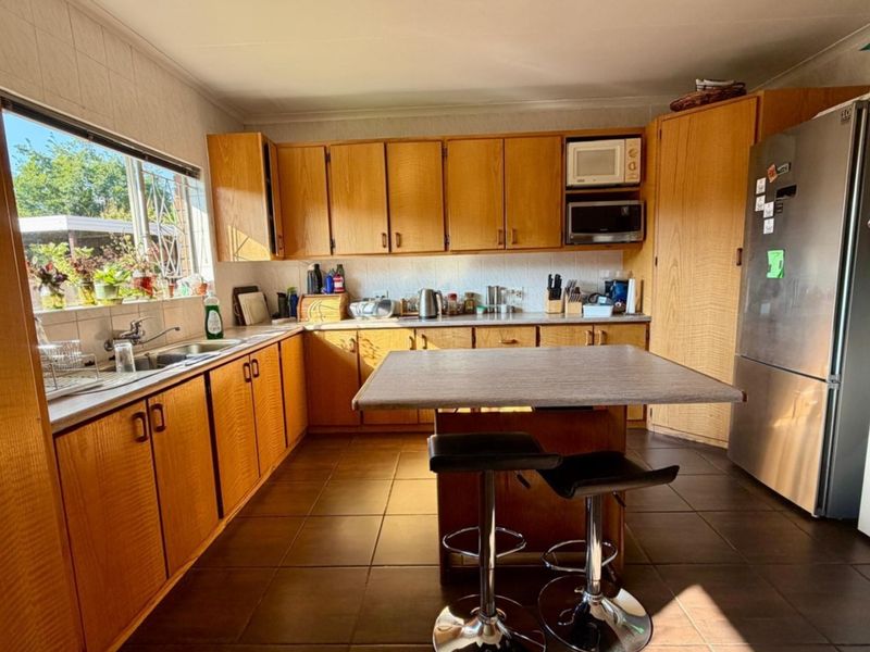 A functional kitchen featuring wood-look laminate cabinetry, tiled flooring, a central breakfast bar, and ample storage space with a tiled backsplash.