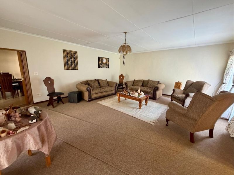 Spacious living room featuring carpeted flooring and a traditional pendant light fixture, offering a blank canvas for modern updates and interior design improvements.