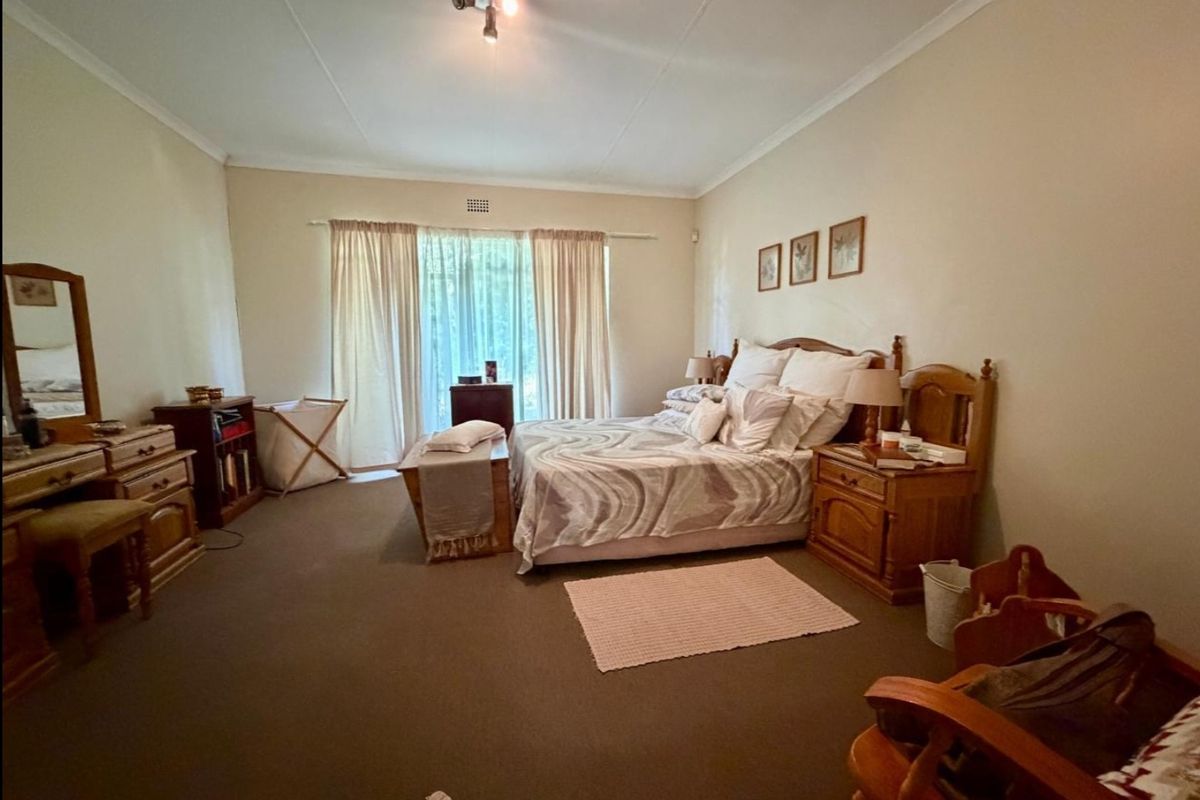 A spacious bedroom featuring neutral wall tones, carpeted flooring, and large windows with curtain treatments, offering a comfortable and functional living space.