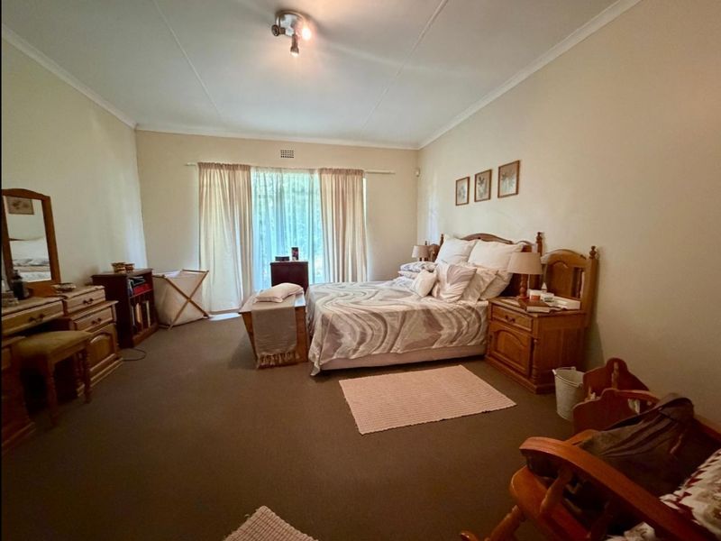 A spacious bedroom featuring neutral wall tones, carpeted flooring, and large windows with curtain treatments, offering a comfortable and functional living space.