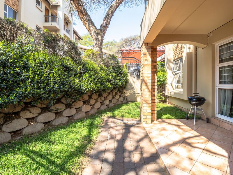 A covered tiled patio area featuring a brick support pillar, adjacent to a small private garden with a stone retaining wall.
