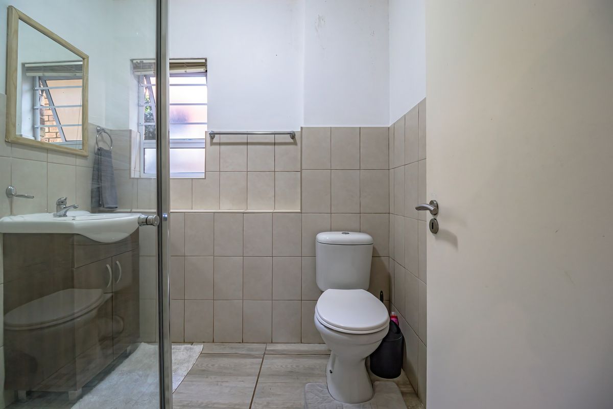 A functional bathroom featuring a vanity cabinet, glass shower enclosure, and neutral wall tiling. The space includes a louvered window for natural ventilation.