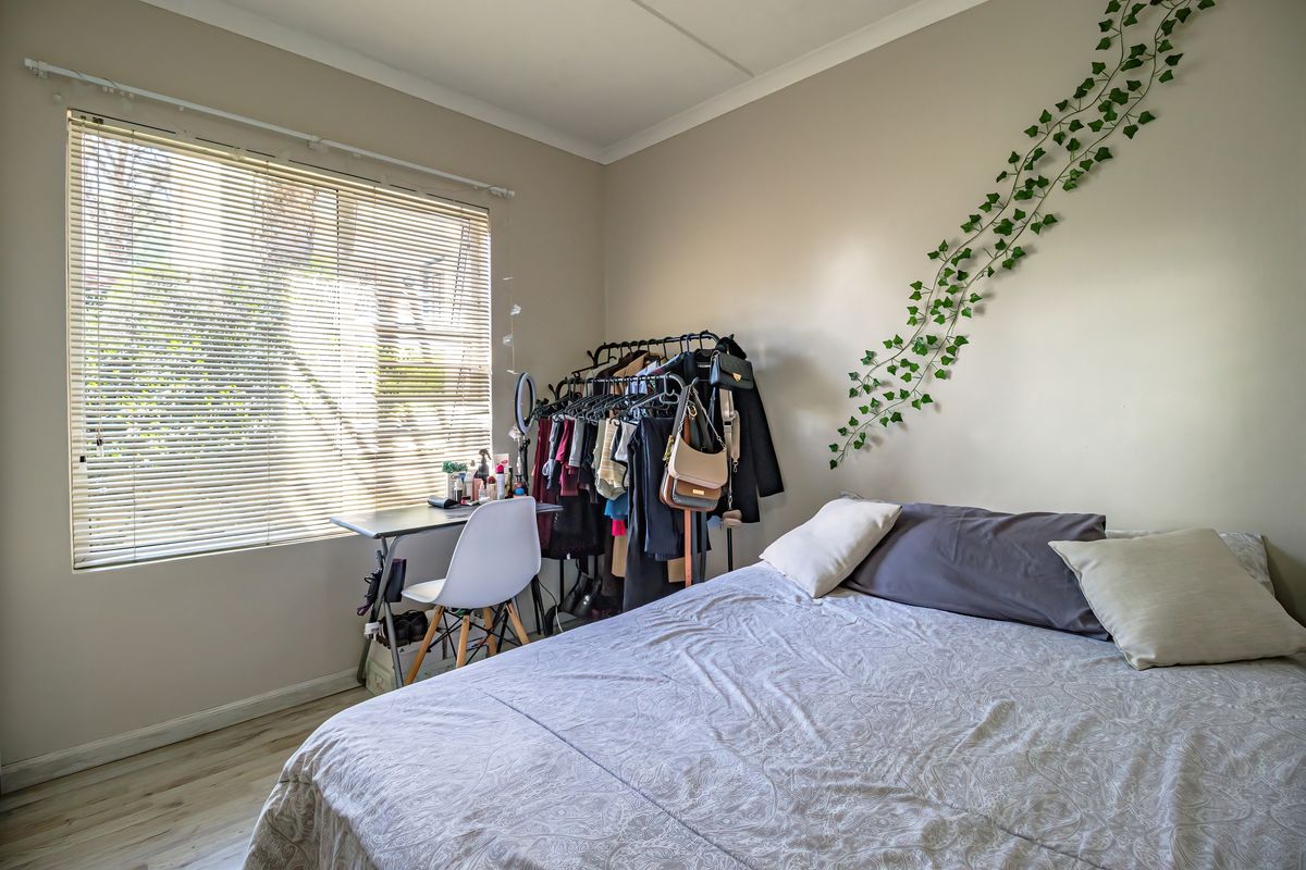 A functional bedroom featuring laminate flooring, neutral wall tones, and venetian blinds allowing natural light into the space.