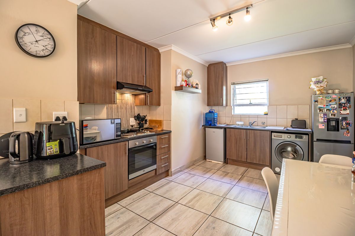 A functional kitchen featuring wood-finish cabinetry, dark laminate countertops, tiled flooring, and integrated appliances including an oven, hob, and extractor fan.