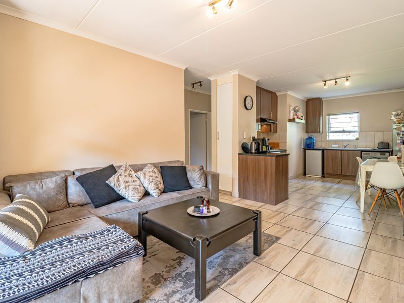 Open-plan living and kitchen area featuring tiled flooring, neutral walls, and functional built-in kitchen cabinetry with an integrated extractor fan.