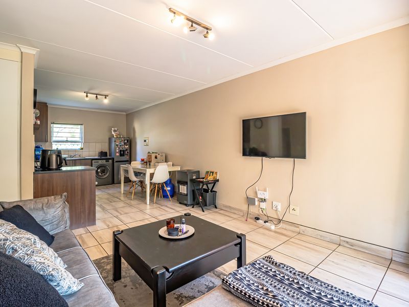 Open-plan living and kitchen area featuring tiled flooring, neutral walls, and functional kitchen cabinetry with integrated sink.