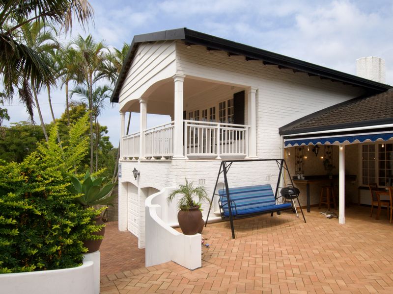 Rear view of the property featuring a paved patio area, a raised balcony with white railings, and a lower-level garage entrance.