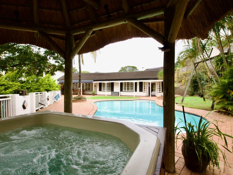 Outdoor entertainment area featuring a swimming pool, a built-in jacuzzi under a thatched gazebo, and brick paved surrounds.