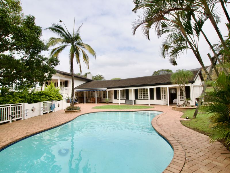 Spacious rear garden featuring a swimming pool, brick-paved patio, and a covered veranda attached to the main residence.