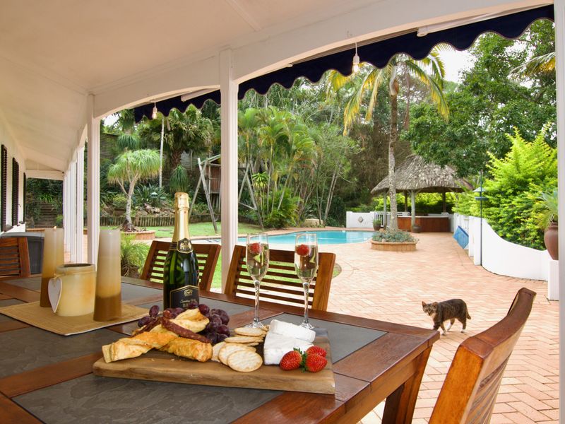 A spacious covered patio overlooking a landscaped garden, swimming pool, and a charming thatched gazebo, perfect for outdoor entertaining.