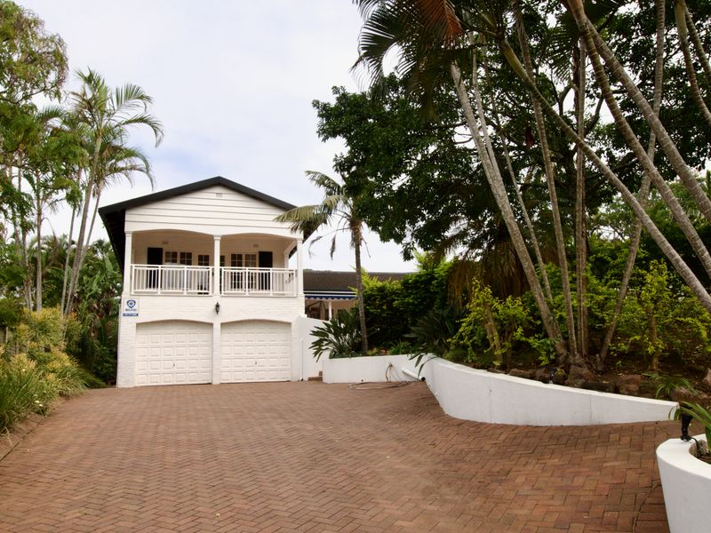 Front elevation of a two-story house featuring a double garage, brick paved driveway, and an upper-level balcony with white timber cladding.