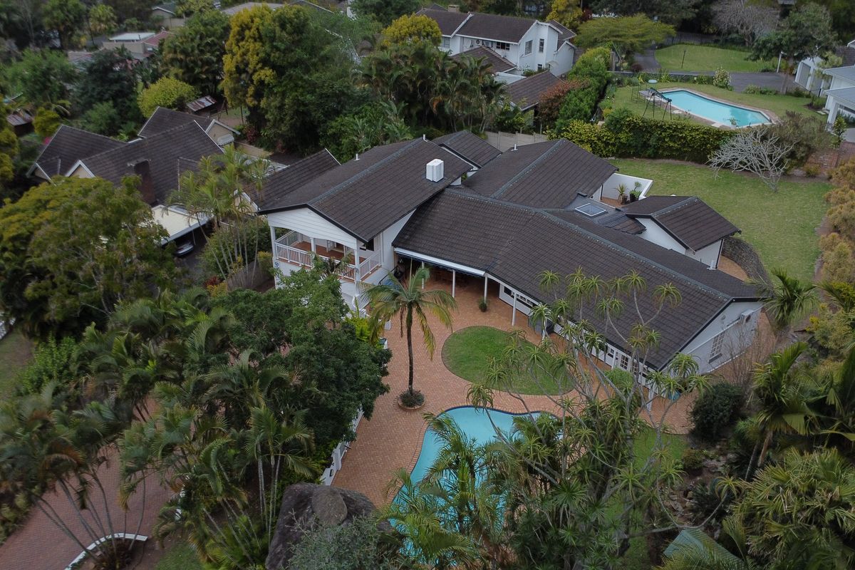 Aerial view of a residential property featuring a large tiled roof, central paved courtyard, swimming pool, and established garden surroundings.