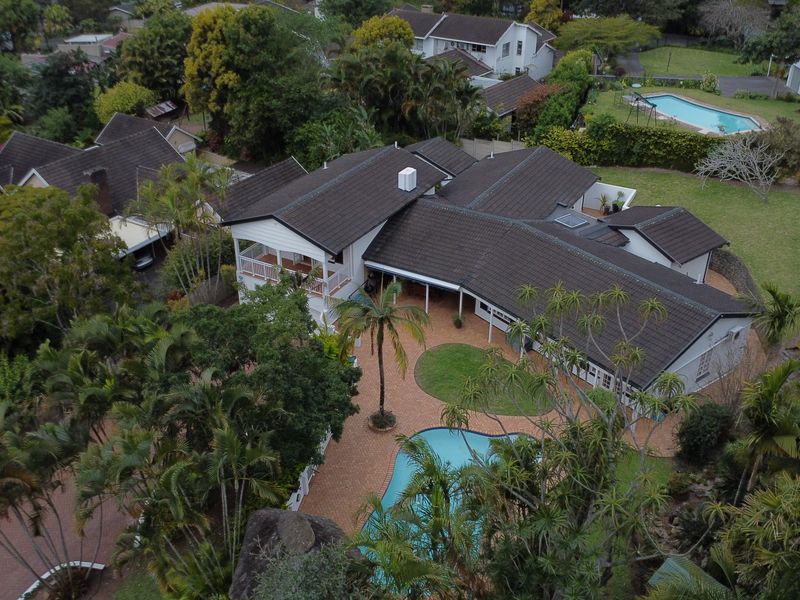 Aerial view of a residential property featuring a large tiled roof, central paved courtyard, swimming pool, and established garden surroundings.