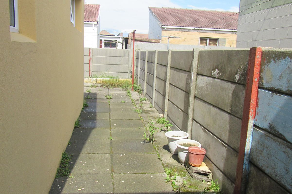 A narrow side passage featuring a paved walkway alongside a precast concrete boundary wall, showing signs of weathering and maintenance requirements.