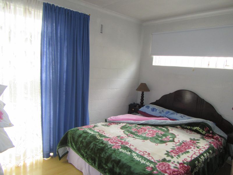 A bedroom featuring laminate flooring, a sliding glass door with curtains, and a horizontal window, providing natural light to the space.