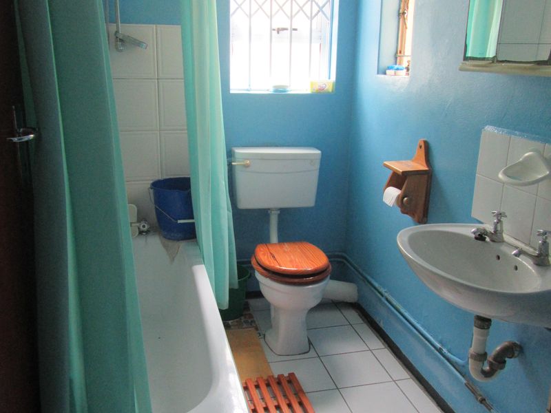 A functional bathroom featuring a bathtub with shower attachment, pedestal sink, and toilet, finished with tiled flooring and blue wall paint.