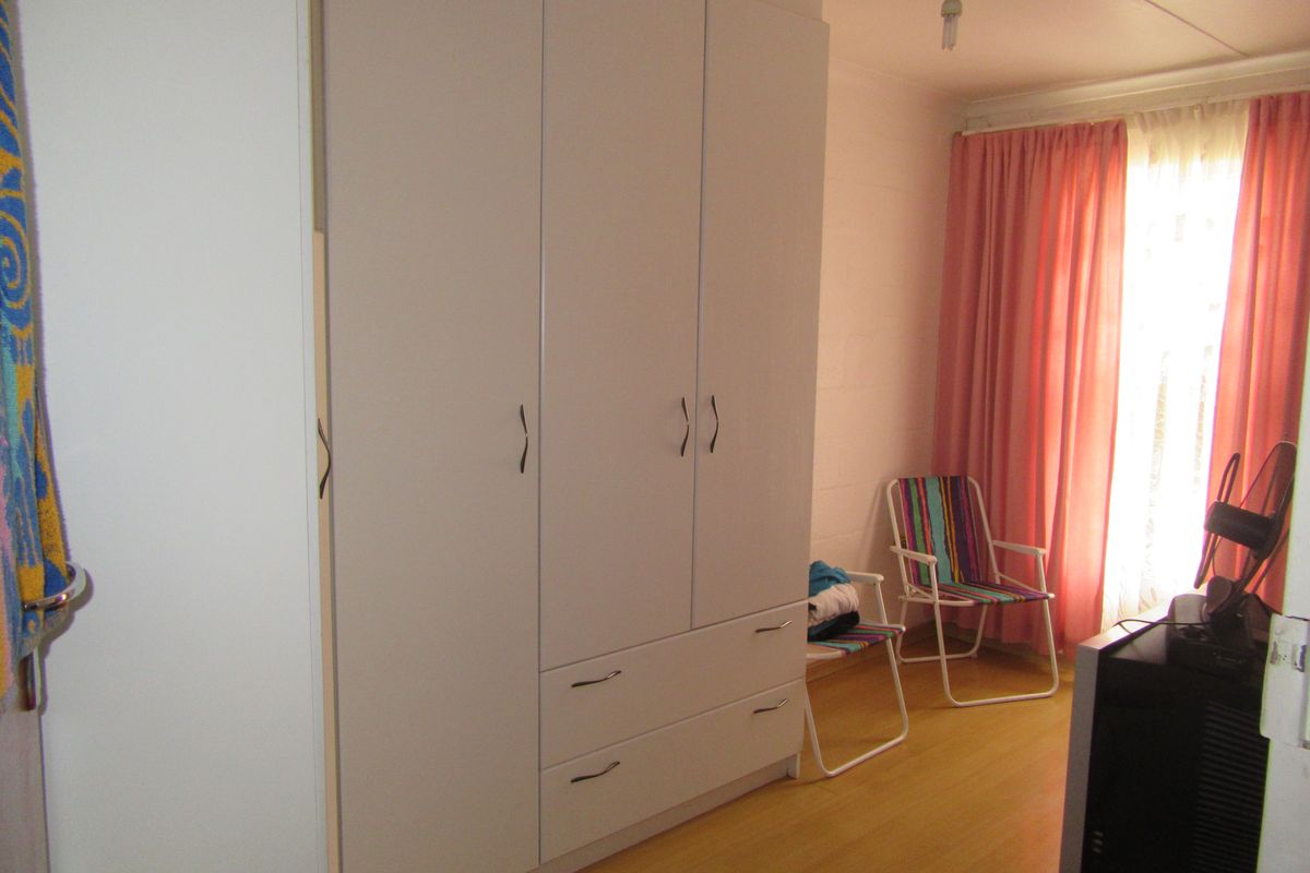 A bedroom featuring a large white built-in wardrobe with integrated drawers and light-toned laminate flooring.