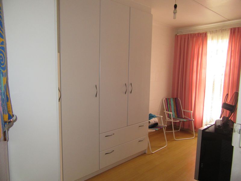 A bedroom featuring a large white built-in wardrobe with integrated drawers and light-toned laminate flooring.