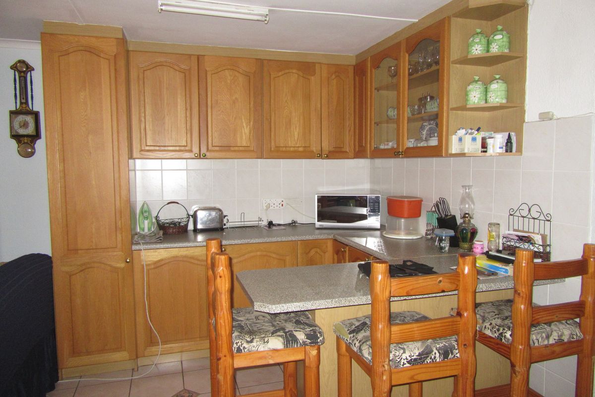 A functional kitchen featuring wooden cabinetry, tiled backsplash, laminate countertops, and an integrated breakfast bar area with tiled flooring.