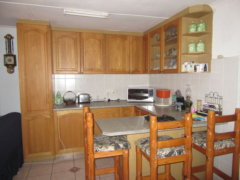 A functional kitchen featuring wooden cabinetry, tiled backsplash, laminate countertops, and an integrated breakfast bar area with tiled flooring.