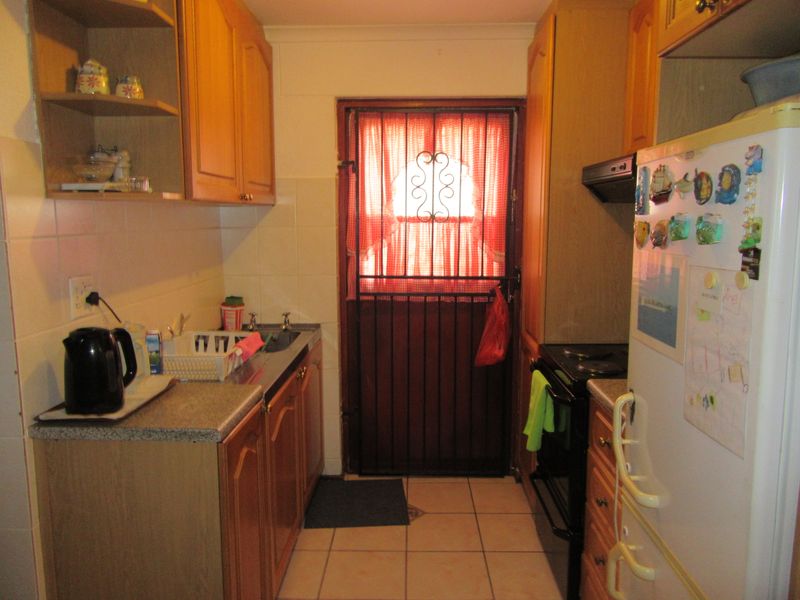 Compact kitchen featuring wooden cabinetry, laminate countertops, tiled splashbacks, and a secure rear access door.
