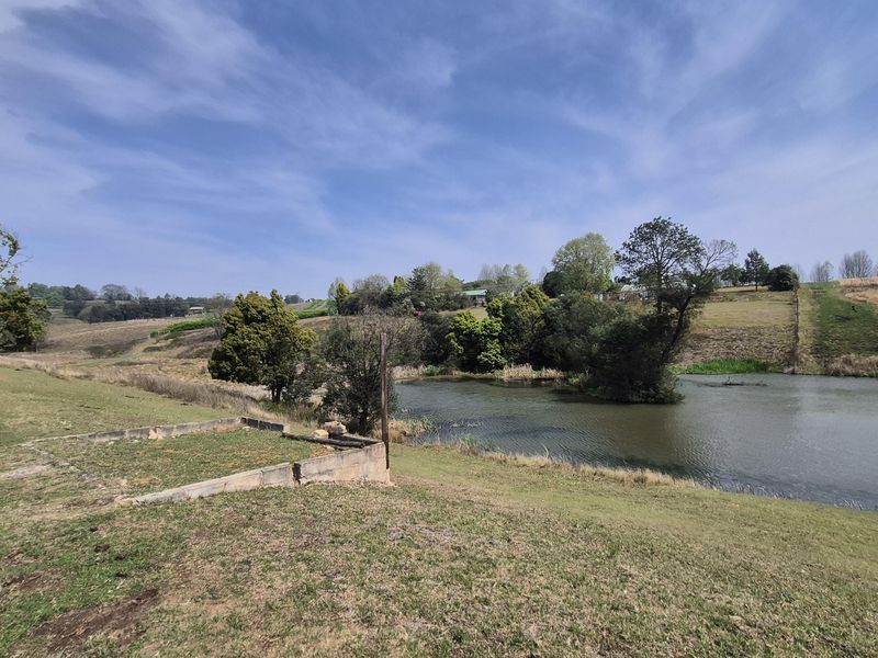 A scenic view of a farm dam with surrounding grassy landscape and a small concrete foundation structure in the foreground.