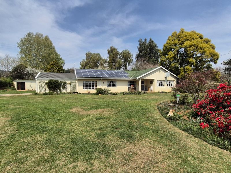 A well-maintained single-story farm residence featuring a large front lawn, established garden, and a roof equipped with solar panels.
