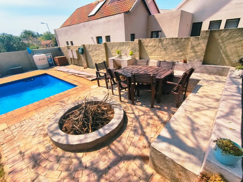 Outdoor pool area featuring a brick-paved patio, built-in fire pit, concrete bench seating, and a functional outdoor wash basin.